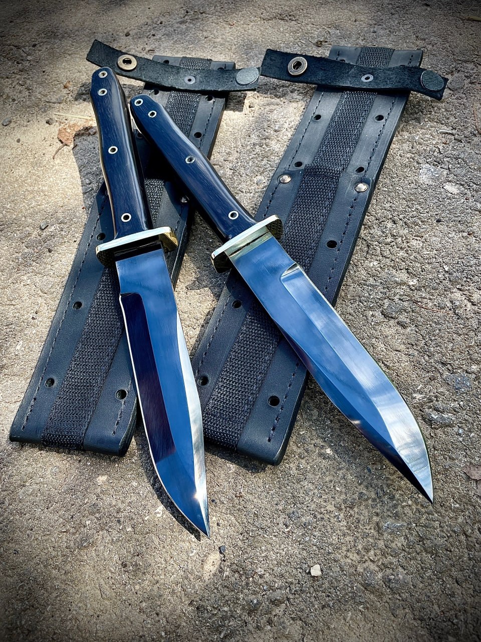 Ножи Warrior Bowie Black Series и их практичные ножны лежат на бетонной поверхности.