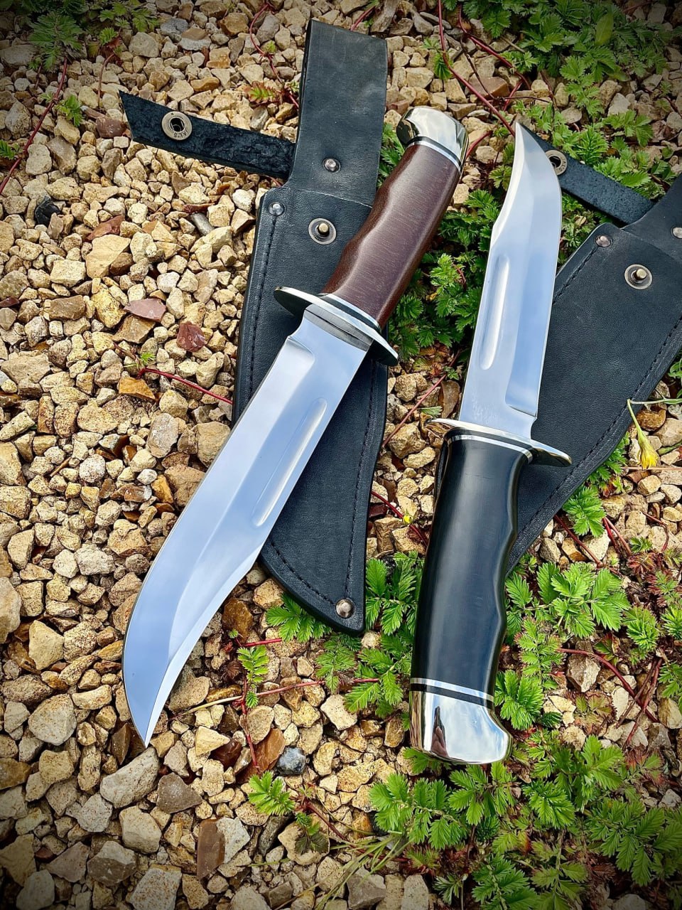 Два ножа Buck 120 General на чёрных кожаных ножнах и щебне: нож с коричневой текстолитовой рукоятью и нож с чёрной рукоятью, большие полированные клинки Боуи
