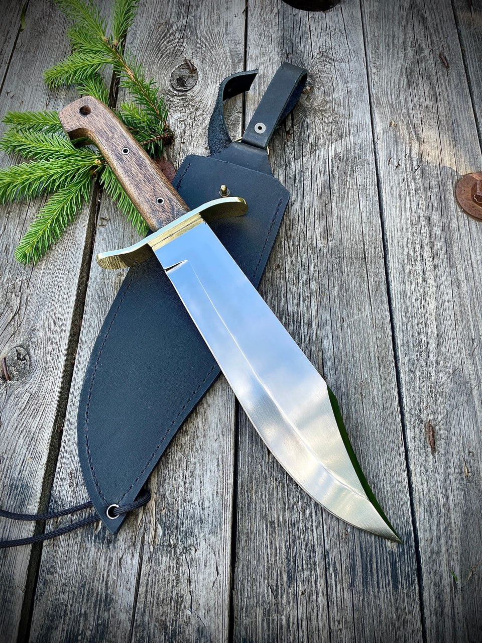 Большой классический нож Wild West Bowie с латунной гардой и кожаными ножнами на деревянном фоне.