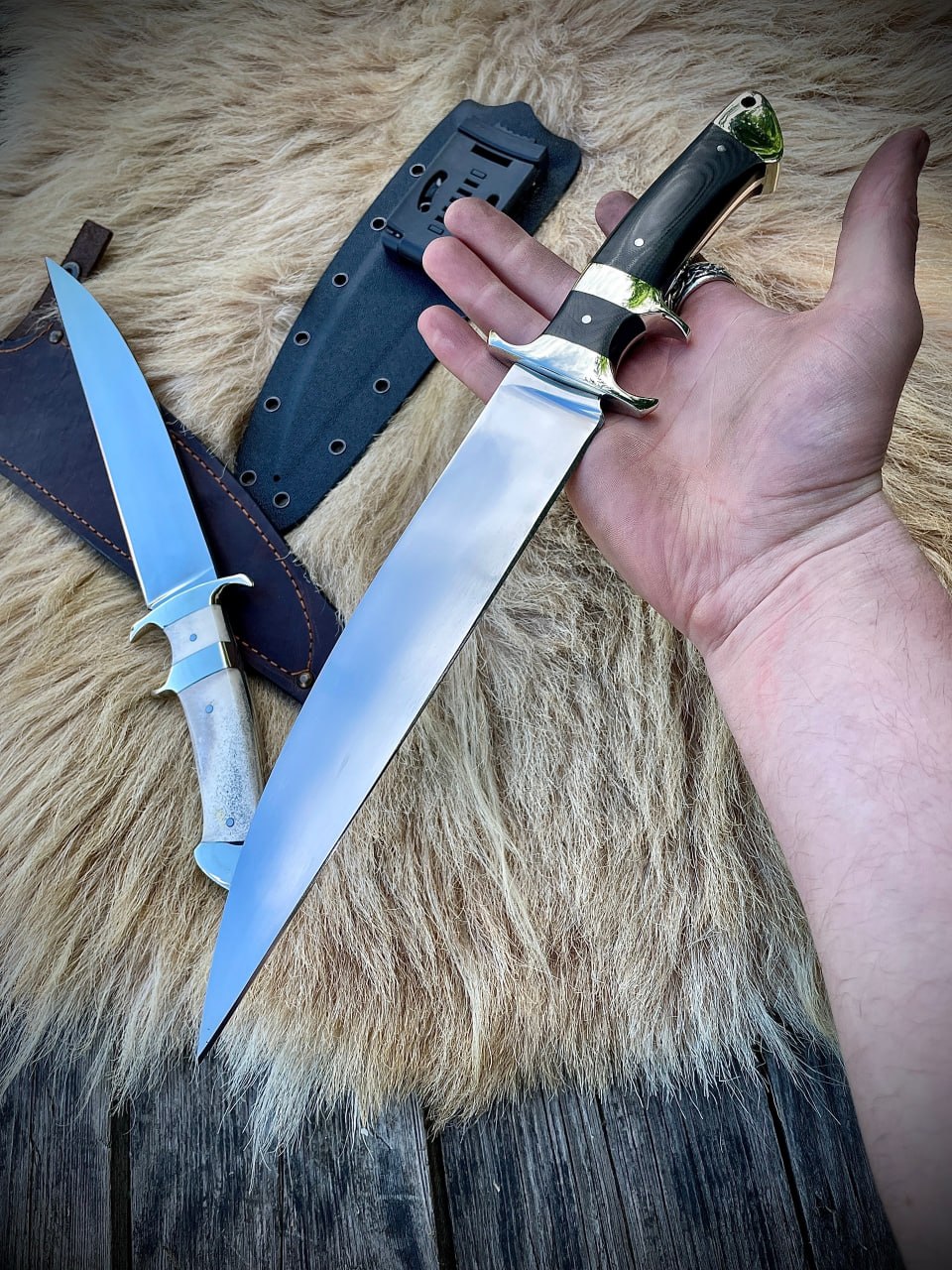 Нож Boar Hunter с черной рукоятью в руке, демонстрирующий размер и эргономику, на меховом фоне.