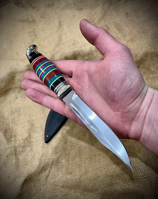 Олдскульная финка без гарды с яркой цветной наборной рукоятью и клинком из стали 95х18 в мужской руке на фоне мешковины.