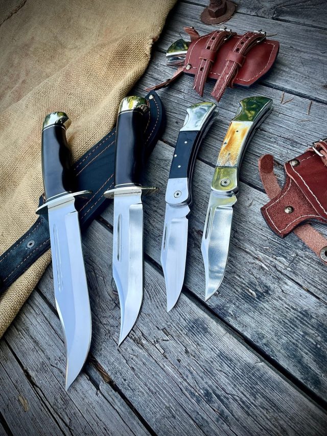 Складные ножи Buck 110 с рукоятями из чёрного G10 и рога лося рядом с охотничьими ножами с чёрными рукоятями на деревянном столе, вокруг — кожаные ножны