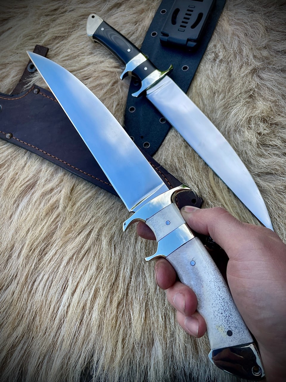 Нож Boar Hunter со светлой рукоятью в мужской руке, на фоне меха и второго ножа с темной рукоятью.