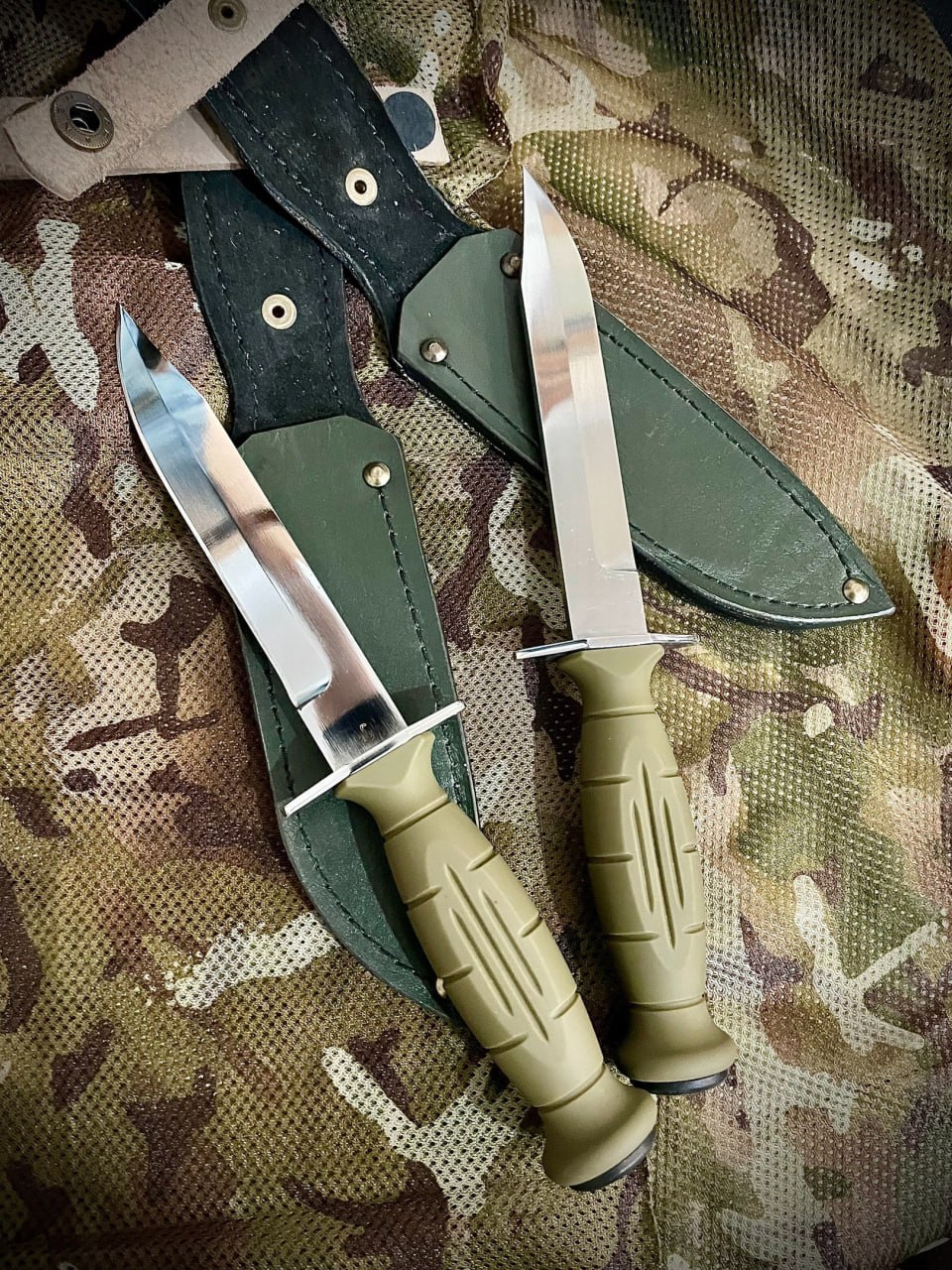 Мощные клинки ножей НР-43 Вишня с прямой гардой и полимерной рукоятью на фоне армейского камуфляжа.