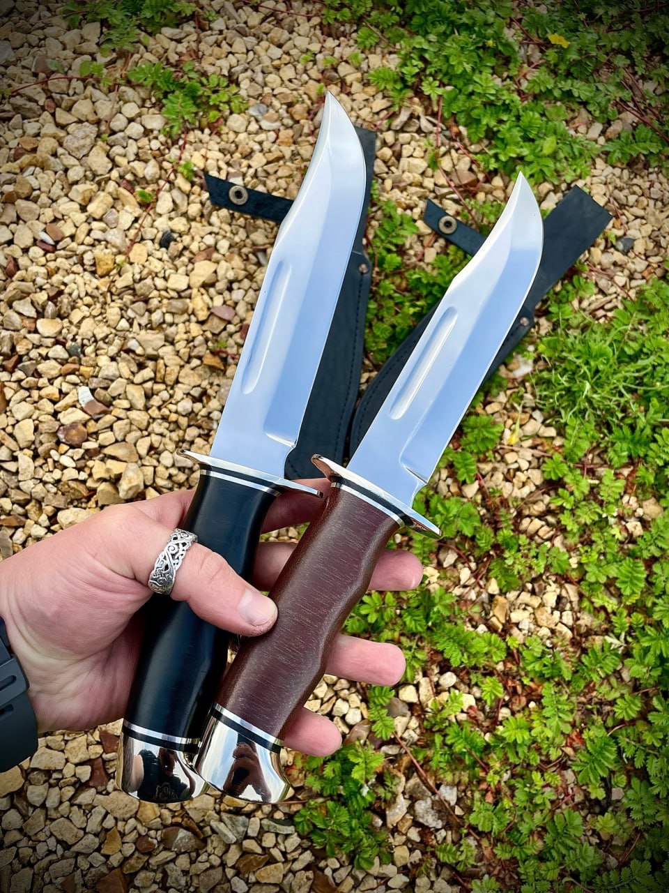 Два ножа Buck 120 General в руке клинками вверх: чёрная и коричневая рукояти с зеркальными навершиями, широкие клинки клип-пойнт с долом